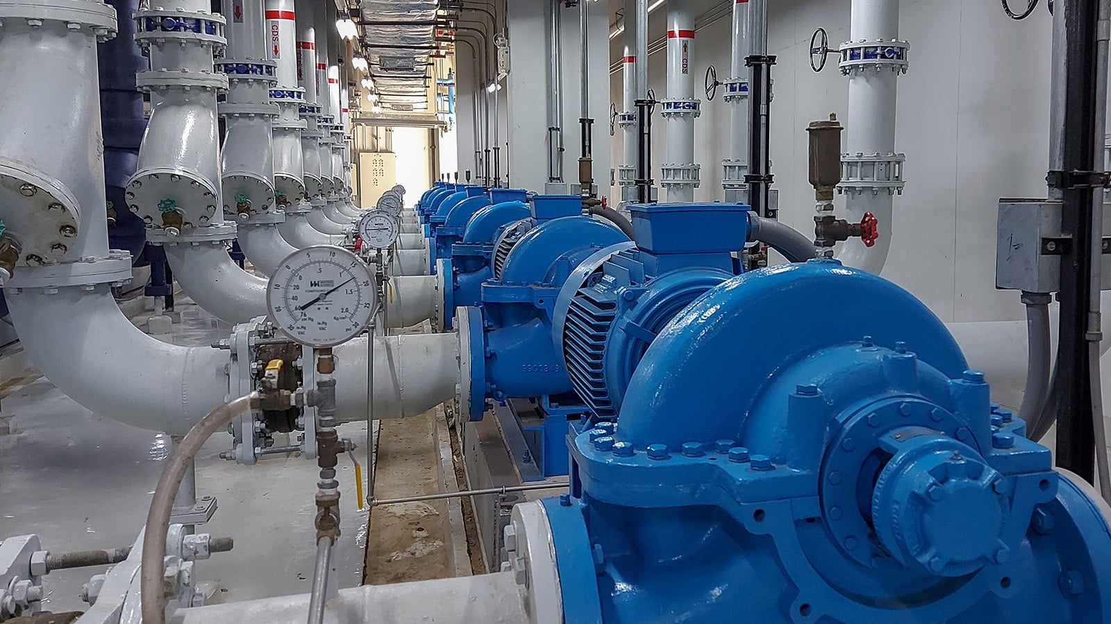 Industrial pump installed in a mechanical equipment room, surrounded by large pipes, valves, and gauges in a commercial facility.