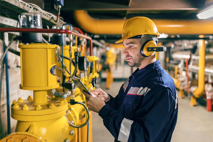 Technician in protective gear checks industrial pumps and other machinery